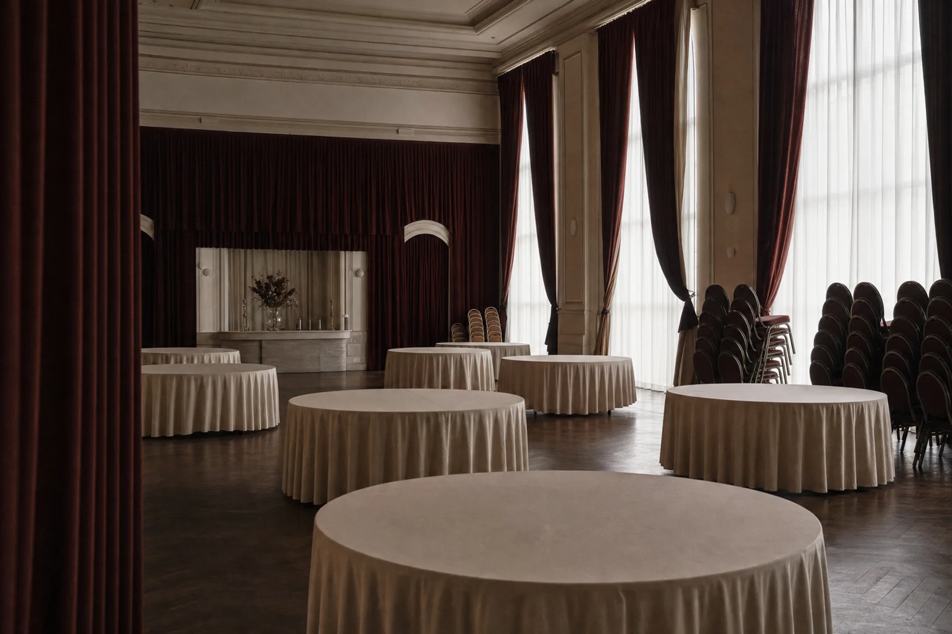 Salle de réception en préparation, tables rondes nappées et chaises empilées.